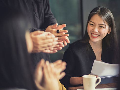 woman sitting at table while several people are clapping